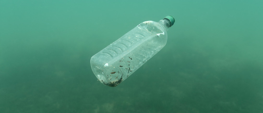 Water bottle filled with debris floating underwater.